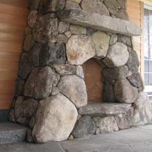 Boulder stone fireplace with antique granite mantel and curved stone hearth